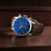 Watch with a blue face and brown leather strap on a wooden surface