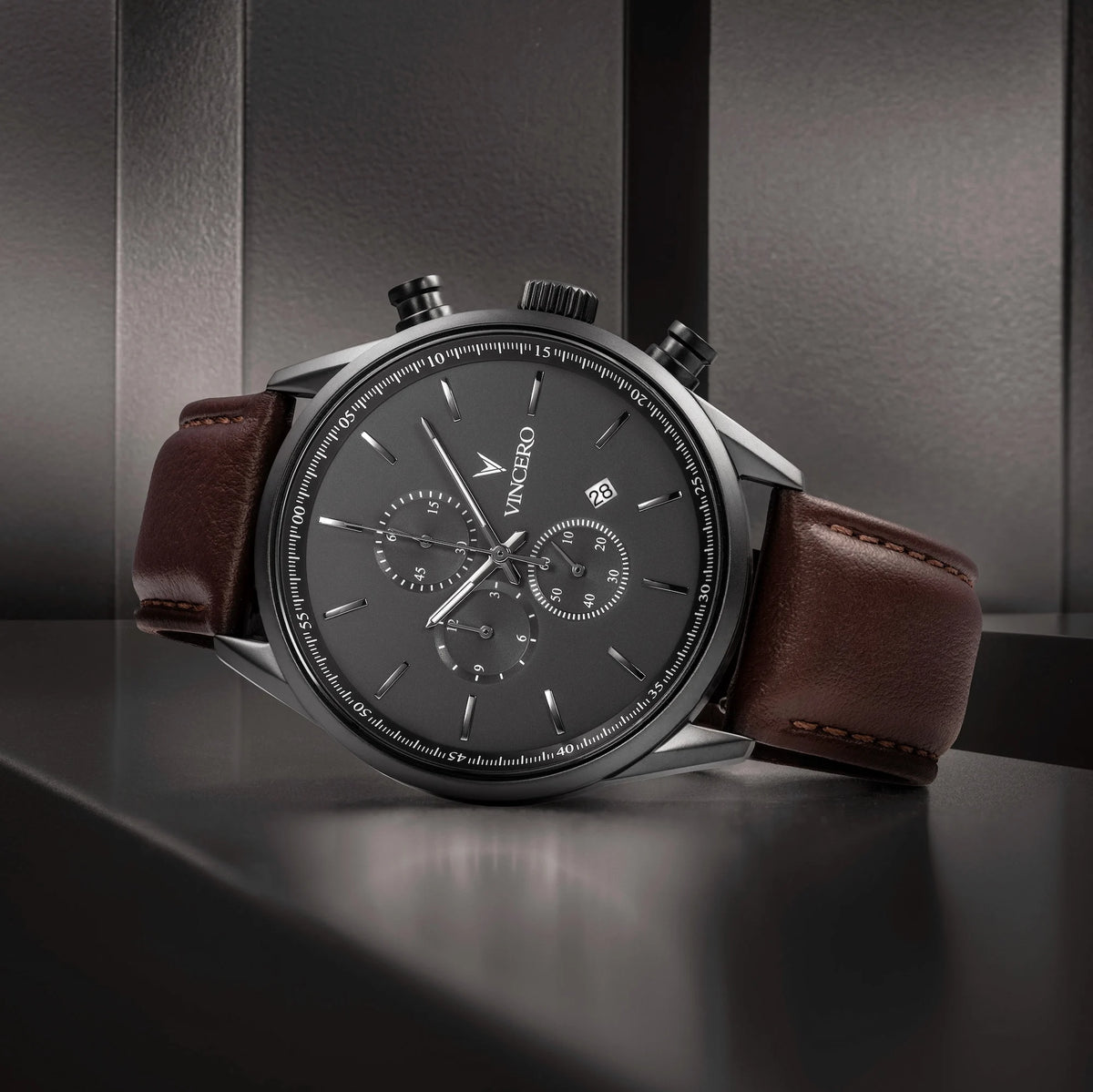 Luxury watch with brown leather strap and black dial on a reflective surface