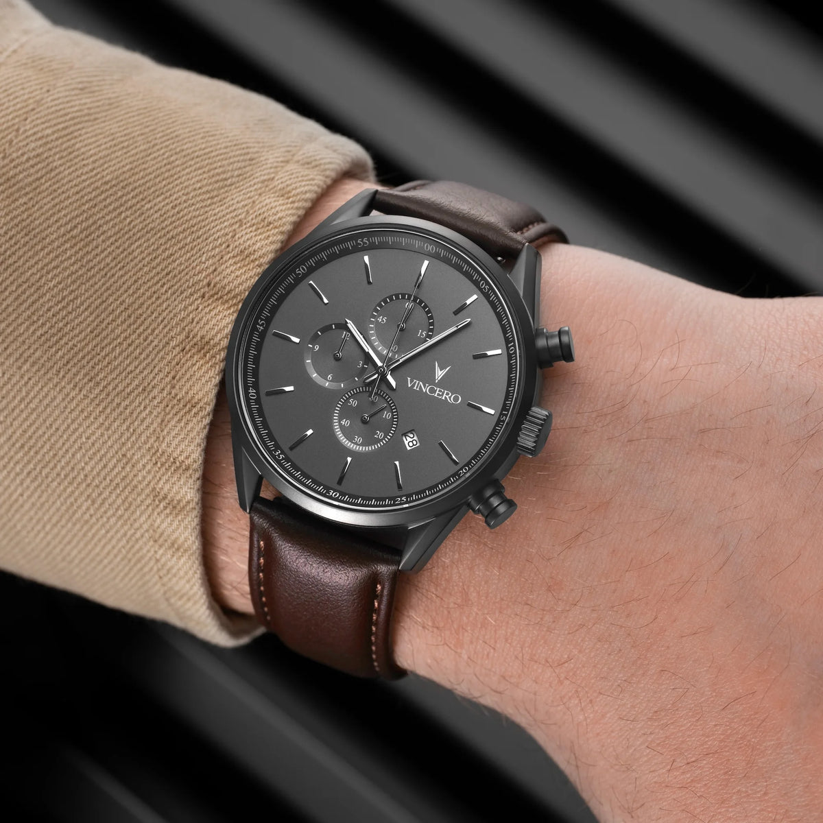 Wrist wearing a watch with a brown leather strap and dark face on a blurred background