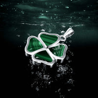 Green four-leaf clover pendant on a dark water surface with light reflections