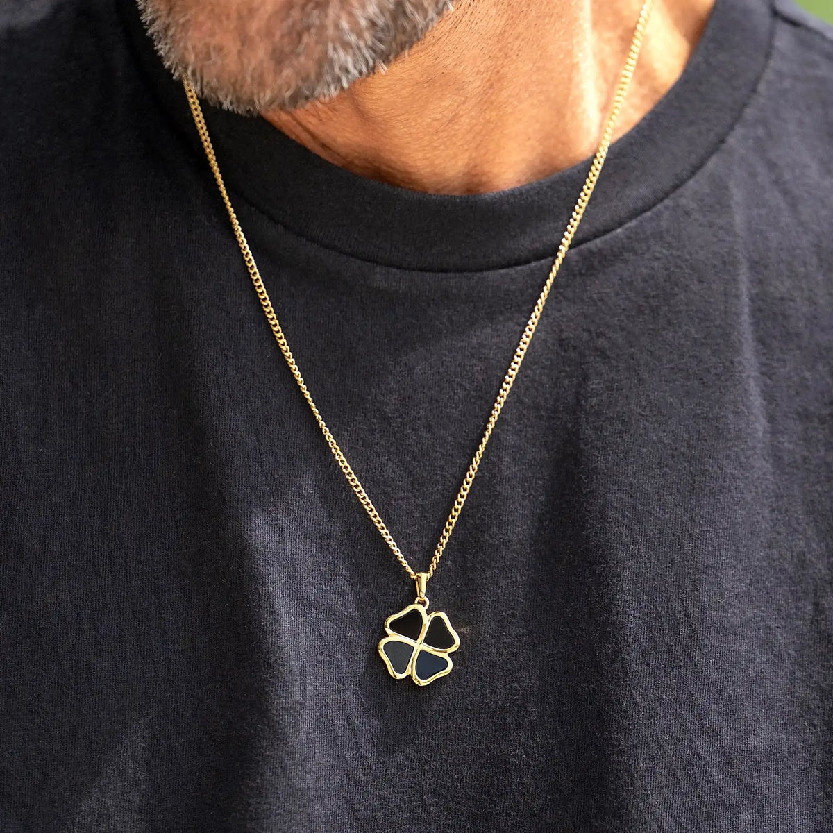 Gold necklace with a clover pendant worn by a person on a black shirt