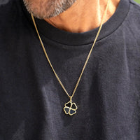 Gold necklace with a clover pendant worn by a person on a black shirt