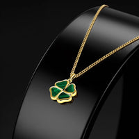 A gold chain necklace with a four-leaf clover pendant featuring green inlay, displayed on a glossy black jewelry bust against a dark background.