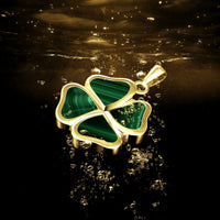 A gold four-leaf clover pendant with green malachite inlay, floating in dark water with bubbles around it.