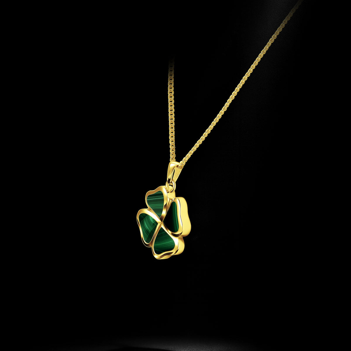 A gold chain necklace with a four-leaf clover pendant featuring dark green stone inlay, shown against a solid black background.