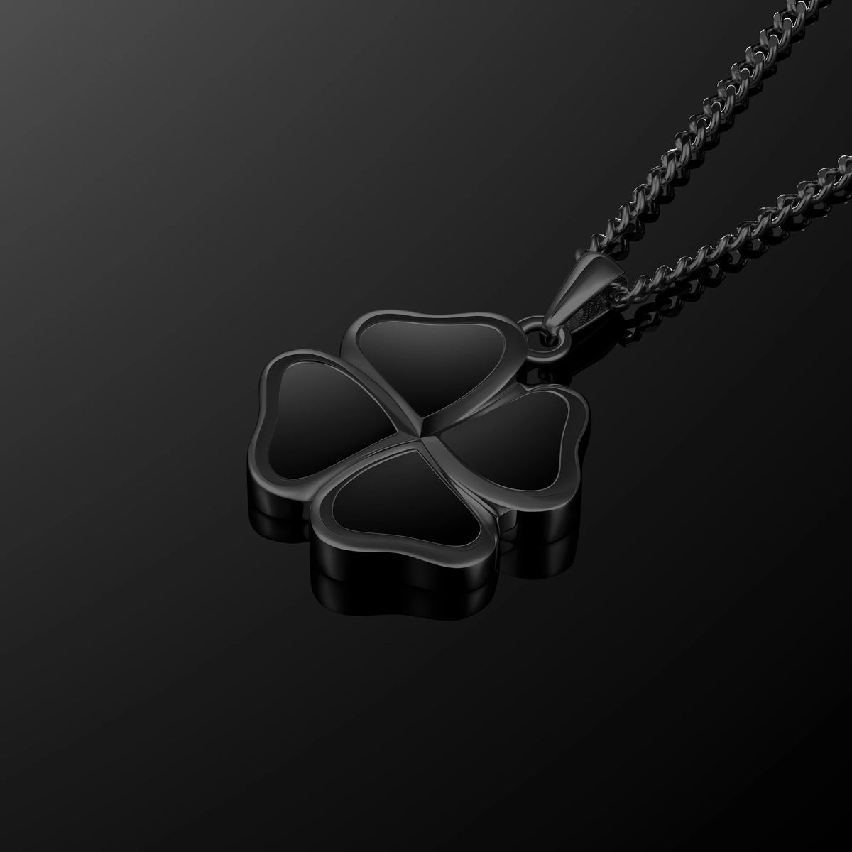 A black four-petal clover pendant necklace on a matching black chain, displayed against a dark reflective background.