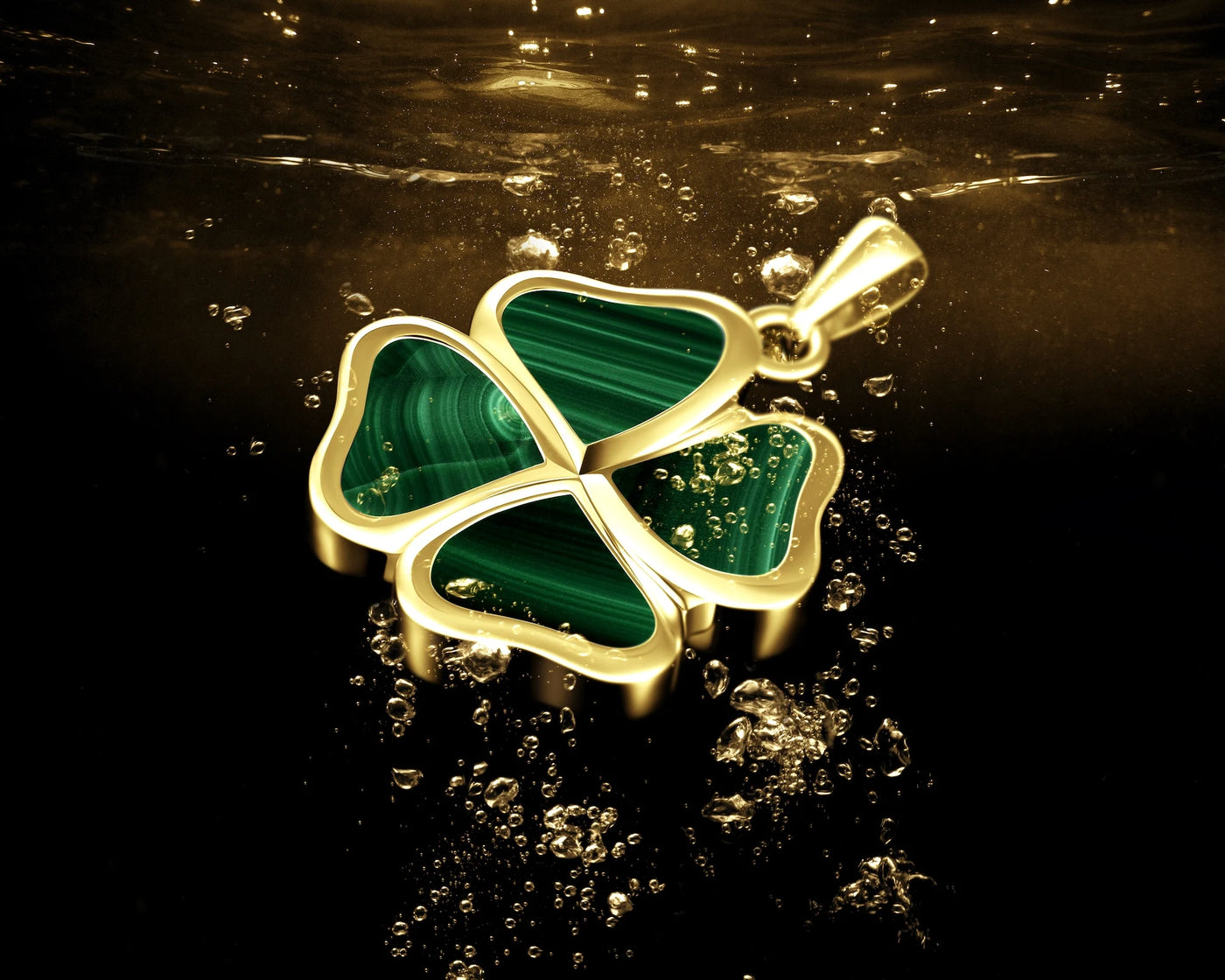 A gold four-leaf clover pendant with green malachite inlay, shown floating in water with bubbles against a dark background.