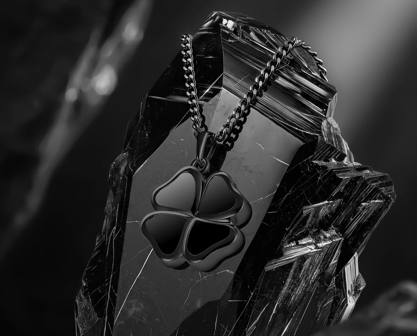 A black metal four-leaf clover pendant necklace on a matching chain, displayed on a faceted dark crystal against a moody black background.