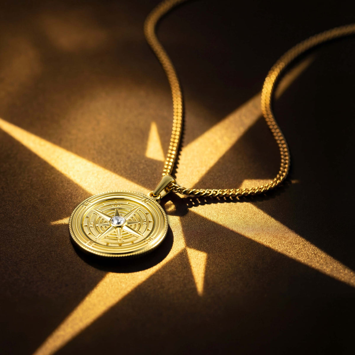 Gold compass necklace on a textured surface with sunlight casting shadows