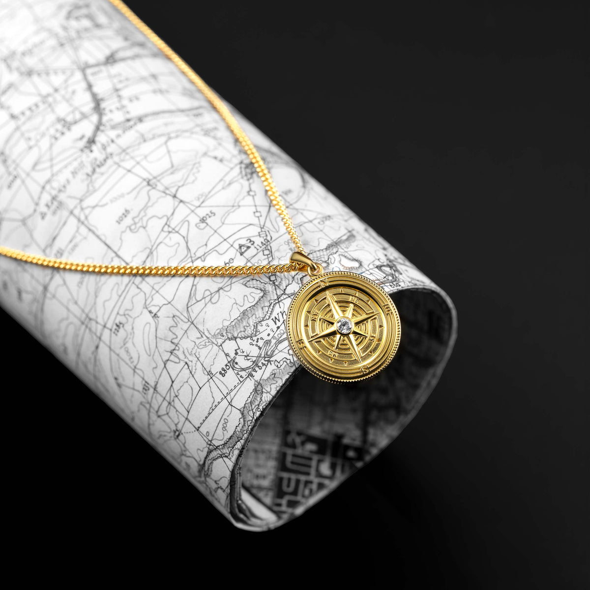 Gold compass necklace on a rolled-up map