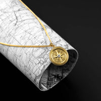 Gold compass necklace on a rolled-up map