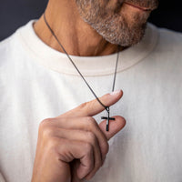 Man holding a necklace with a cross pendant against a neutral background