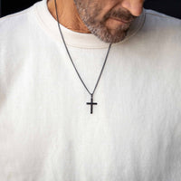 Man wearing a white sweater with a black cross necklace.