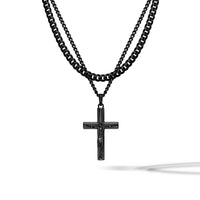 A double-strand black metal necklace featuring a curb chain and a smaller link chain with a dark cross pendant containing a figure, shown against a plain white background.