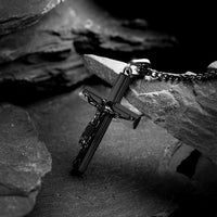 Black crucifix pendant for man leaning on rock. 
