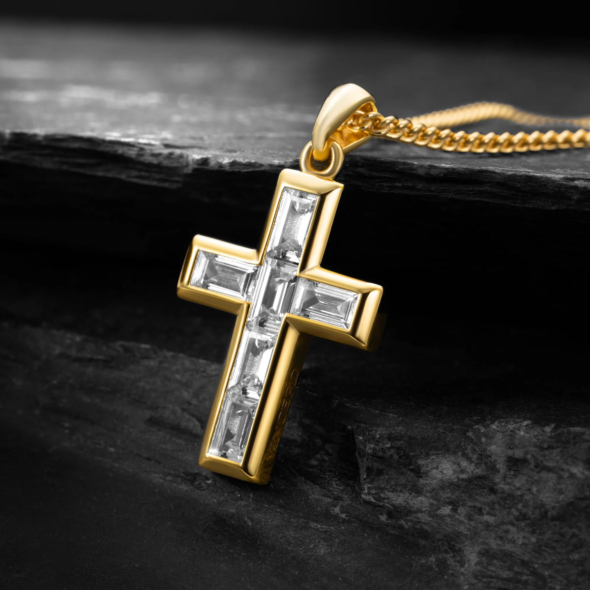 Gold cross pendant with clear stones on a dark stone surface