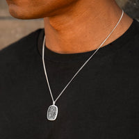 Silver necklace with a pendant worn by a person against a black shirt background