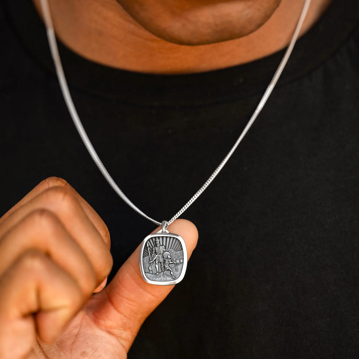 Silver necklace with a pendant held by a hand against a black background