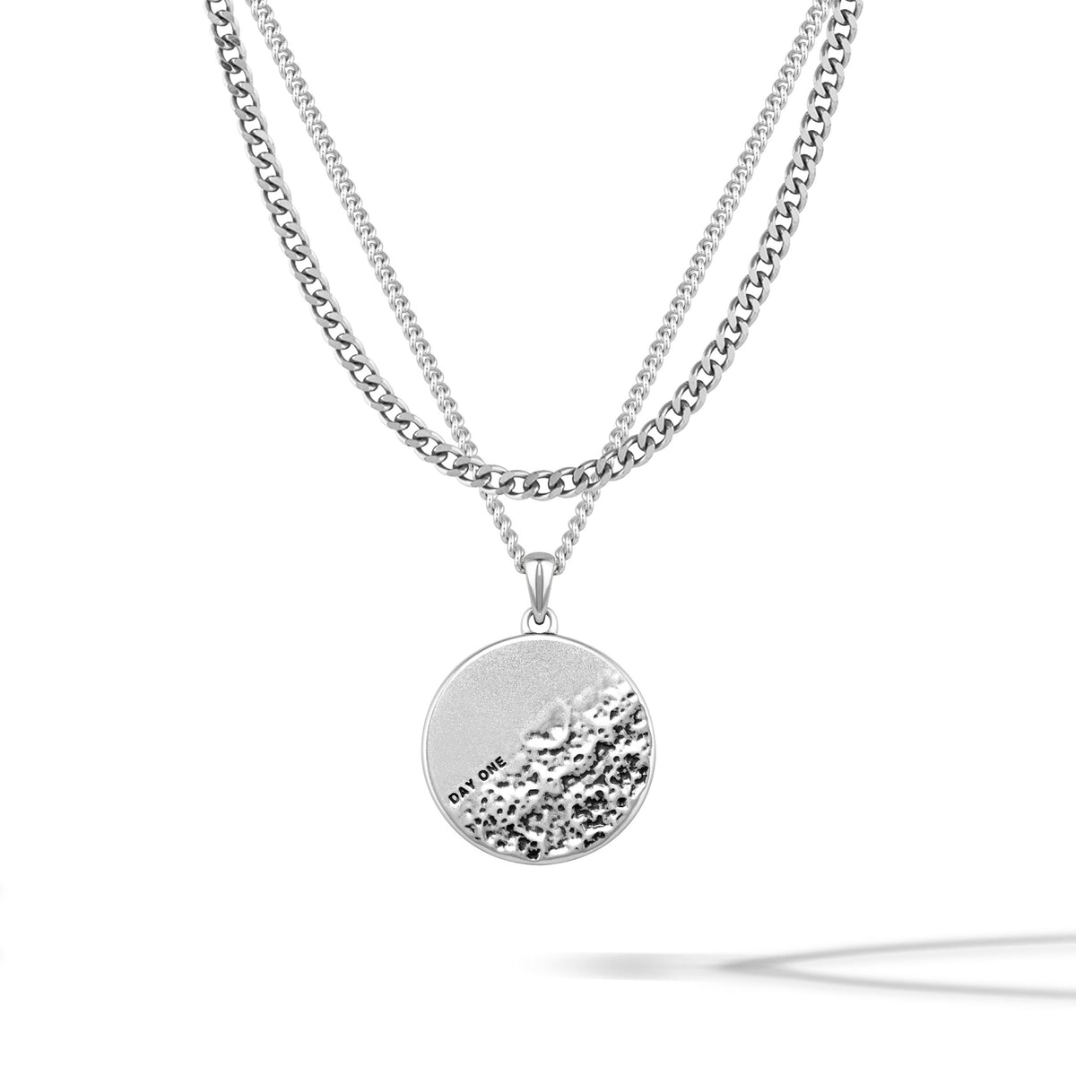 A sterling silver pendant necklace with a rough and smooth surface on a chain, representing life's challenges and successes.