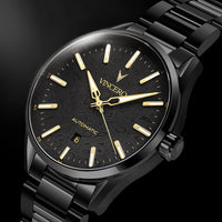 A close-up of a VINCERO automatic watch with a black textured dial, gold-tone hands and indices, and a black metal link bracelet, set against a dark background.