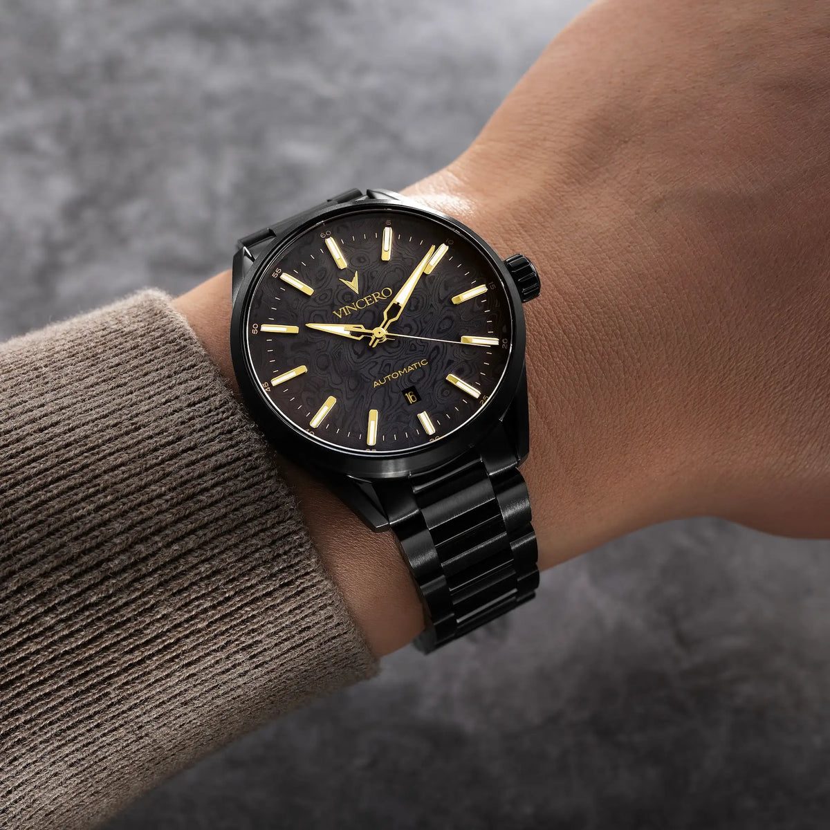 A black Vincer wristwatch with a black metal link bracelet and gold-tone hands and indices, shown worn on a person's wrist.