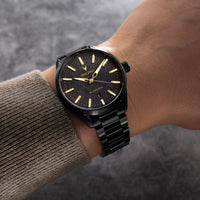 A black Vincer wristwatch with a black metal link bracelet and gold-tone hands and indices, shown worn on a person's wrist.