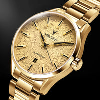 A gold-tone automatic watch by Vincero, featuring a textured, patterned dial and a matching gold-tone metal link bracelet, set against a dark background.
