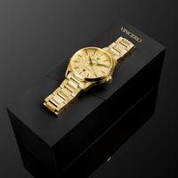 A gold-tone Vincero watch with a textured dial and matching gold-tone metal bracelet, displayed diagonally on top of a black presentation box against a dark background.