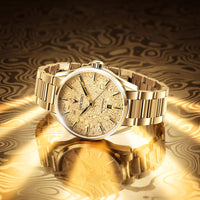 A gold-tone stainless steel wristwatch with a patterned dial and matching gold bracelet, displayed on a reflective gold surface with a dark patterned background.
