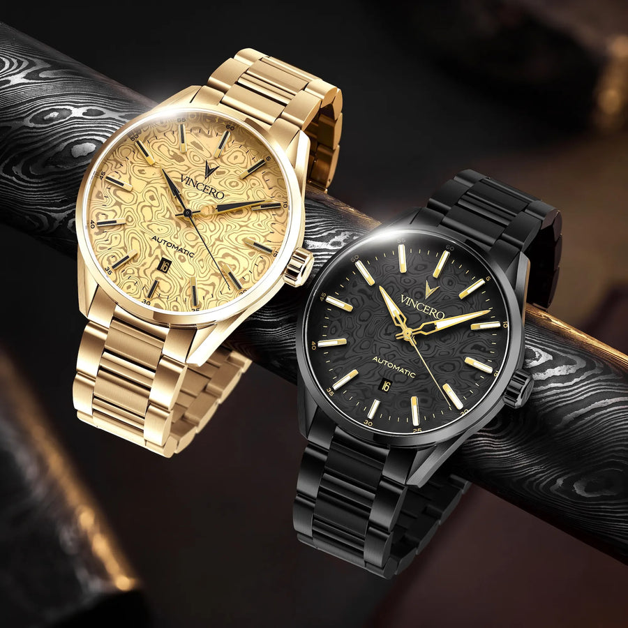 Two Vincero automatic wristwatches displayed on a dark textured surface. One watch has a gold-tone case and a gold dial with a swirling pattern, paired with a gold-tone link bracelet.
