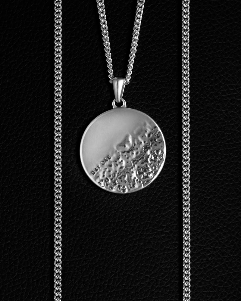 A sterling silver pendant necklace with a rough and smooth surface on a chain, representing life's challenges and successes.