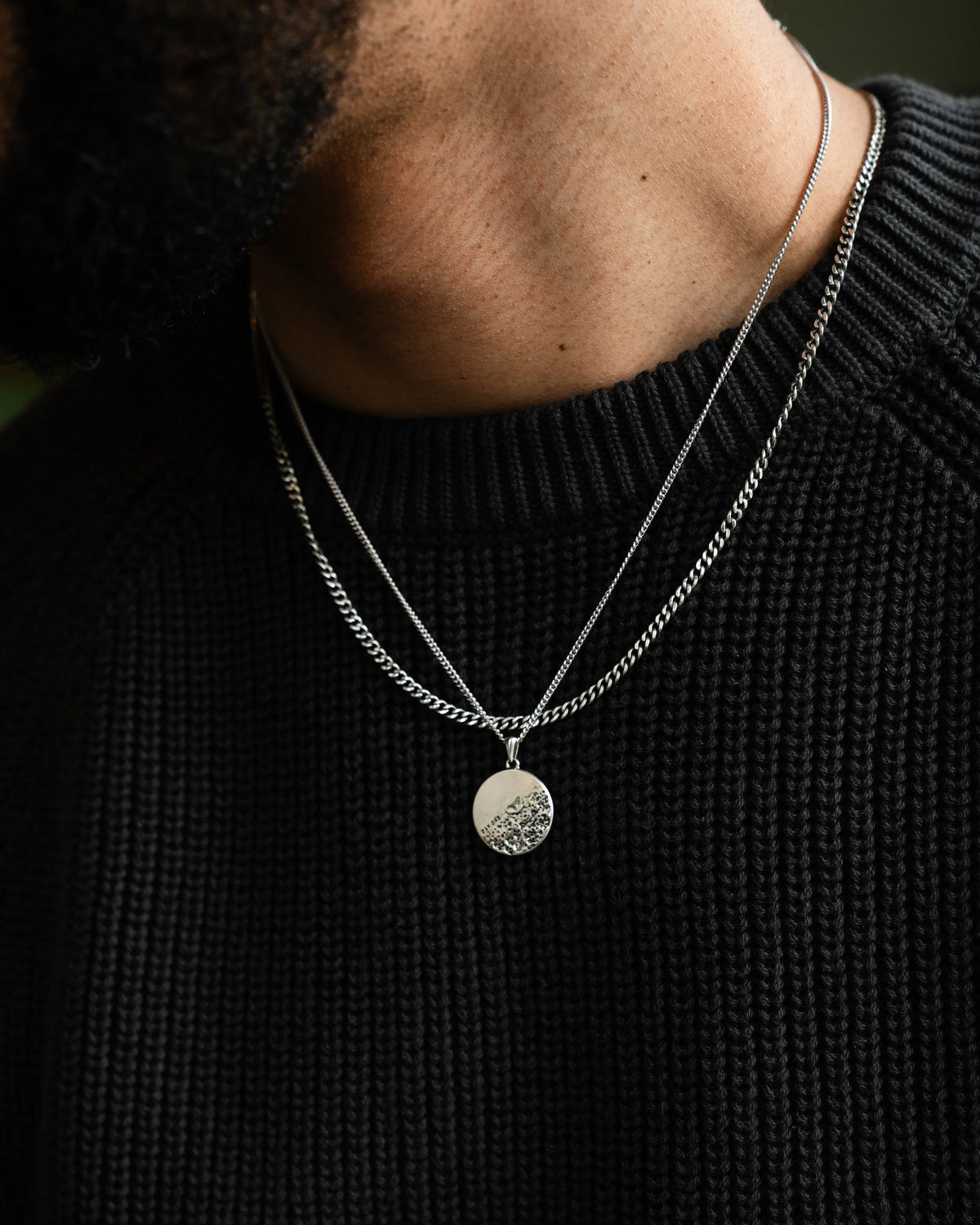 A sterling silver pendant necklace with a rough and smooth surface on a chain, representing life's challenges and successes.