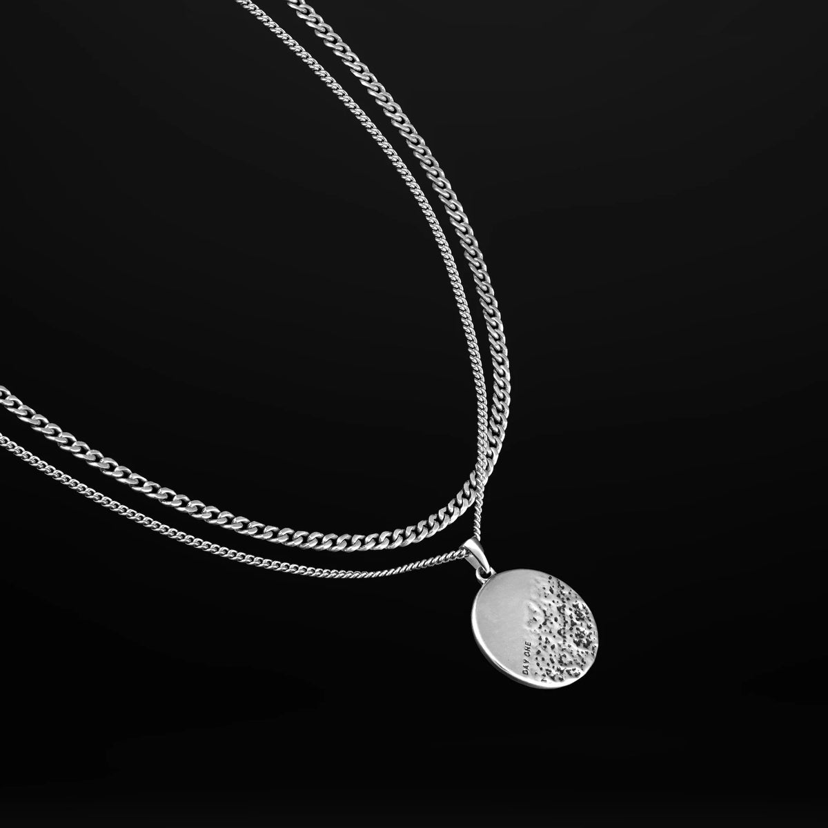A sterling silver pendant necklace with a rough and smooth surface on a chain, representing life's challenges and successes.