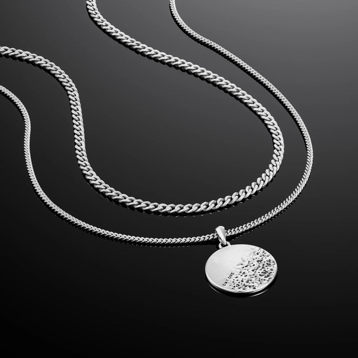 A sterling silver pendant necklace with a rough and smooth surface on a chain, representing life's challenges and successes.