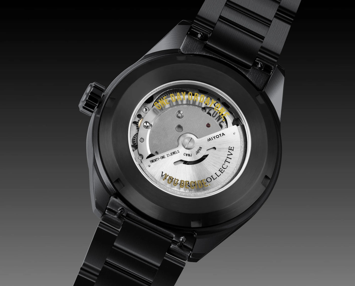Close-up of a black analog watch with a transparent case back, showing the silver-toned mechanical movement and gold text, on a dark gradient background.