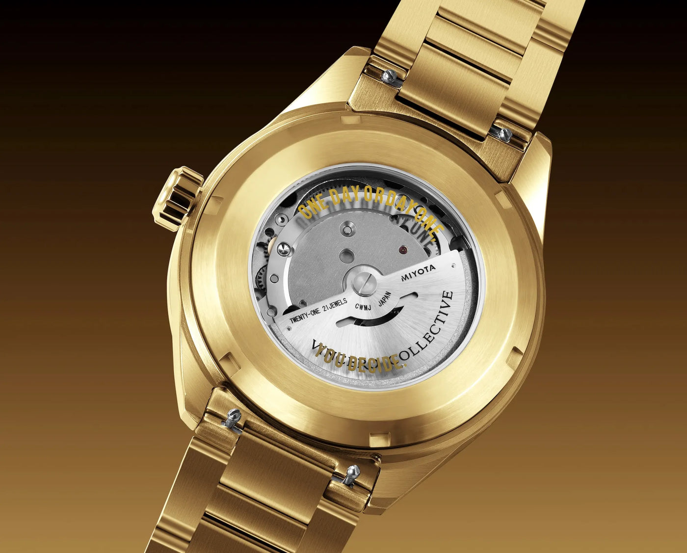 Close-up of a gold-tone wristwatch showing the transparent back case and internal mechanical movement. The brand name JIYOTA is visible on the inner dial, with additional text reading WSBRO Collective.