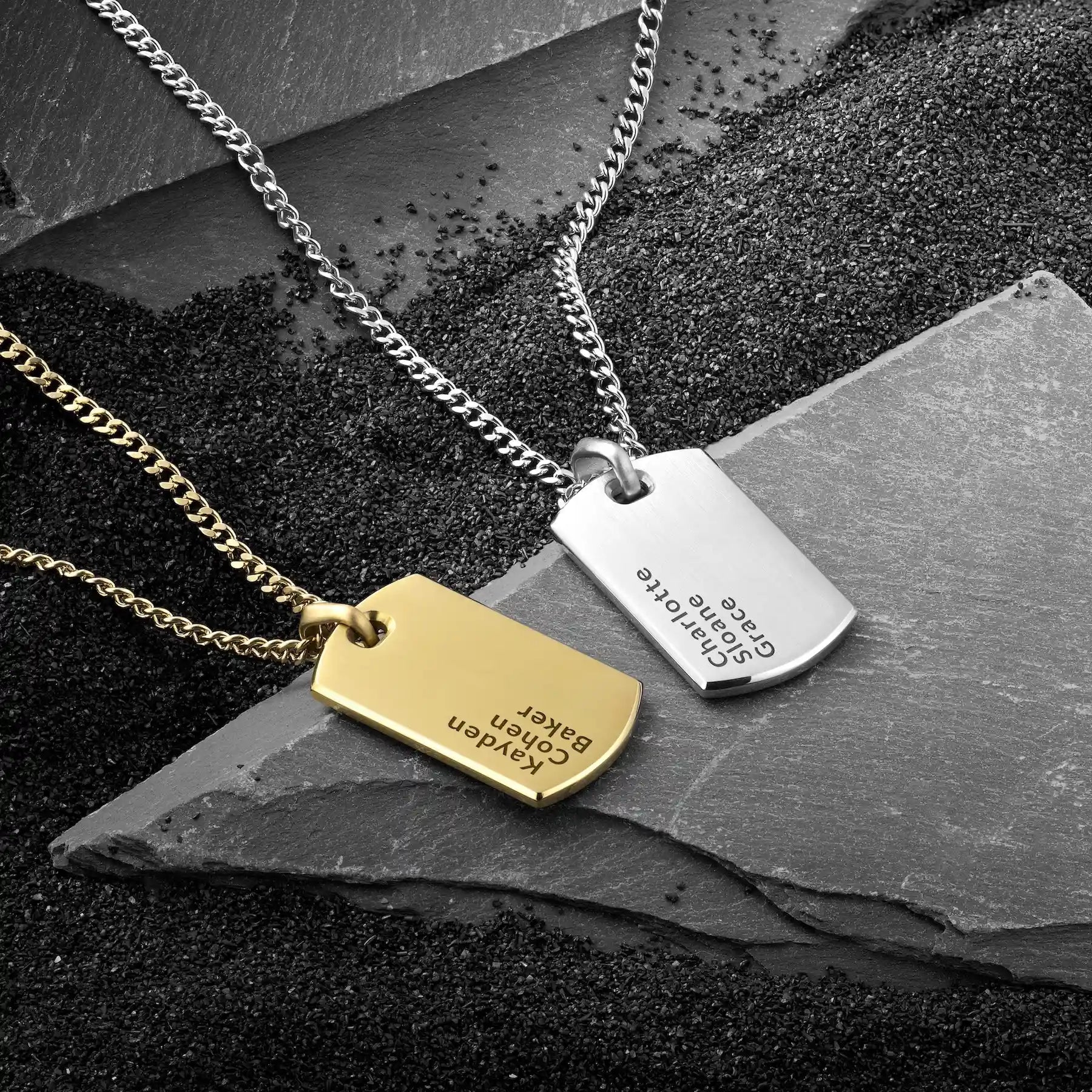 Two necklaces with engraved tags on a dark stone surface