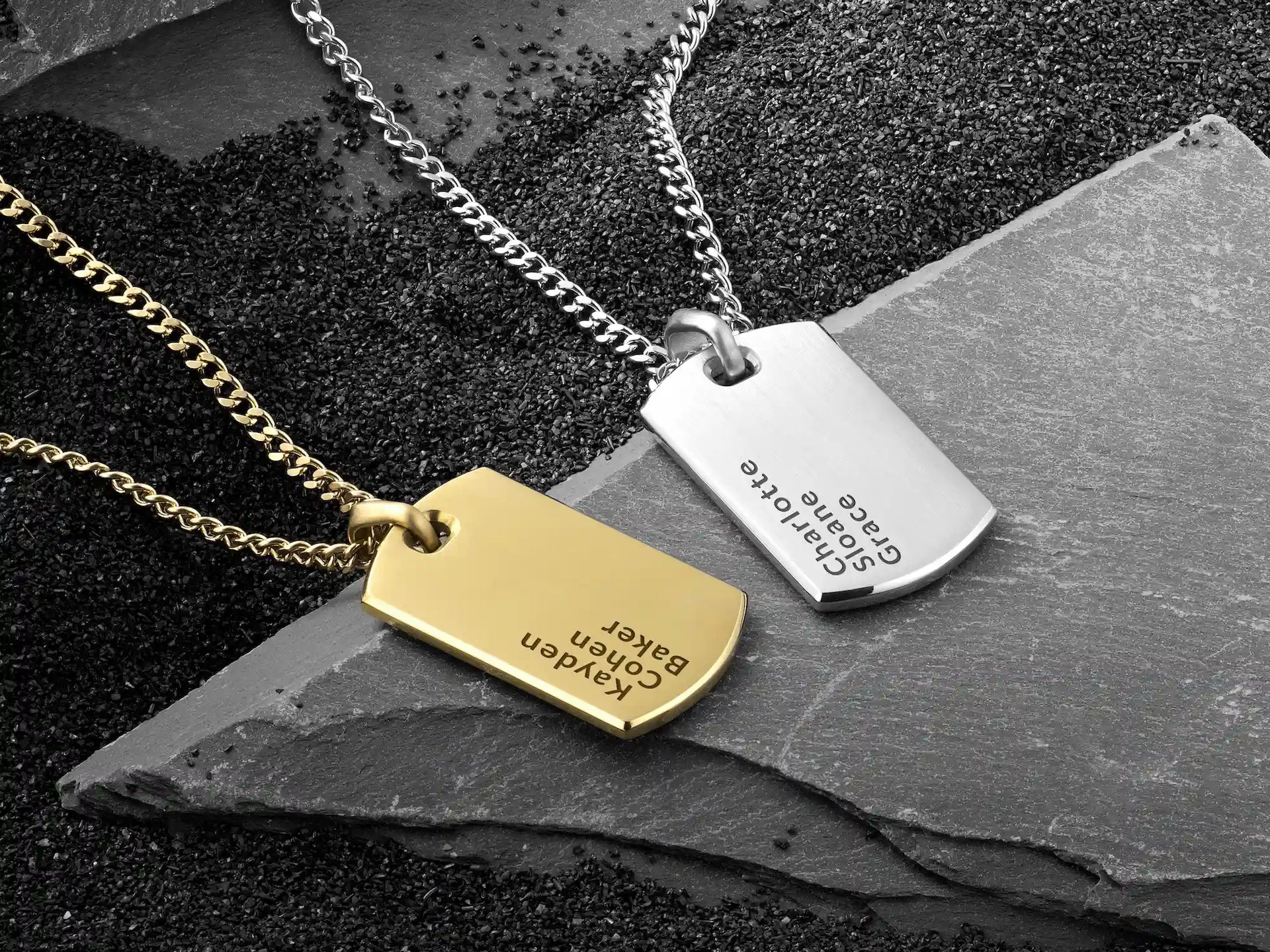 Two necklaces with engraved tags on a dark stone surface