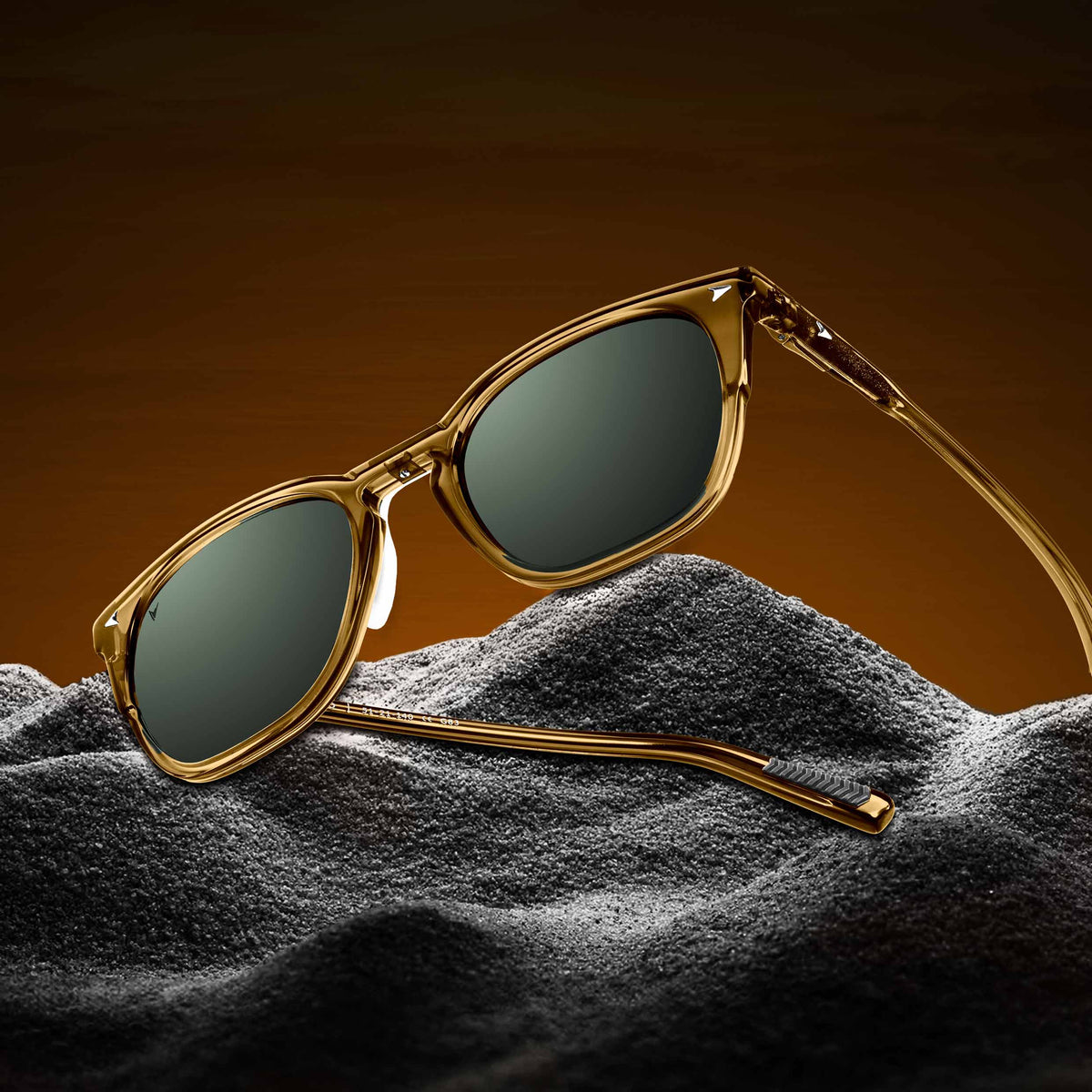 Gold-framed sunglasses with dark lenses on a textured surface against a gradient background
