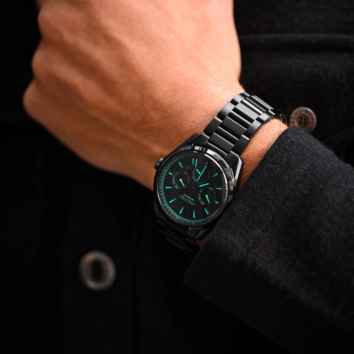 Black watch with green face on a wrist against a dark background