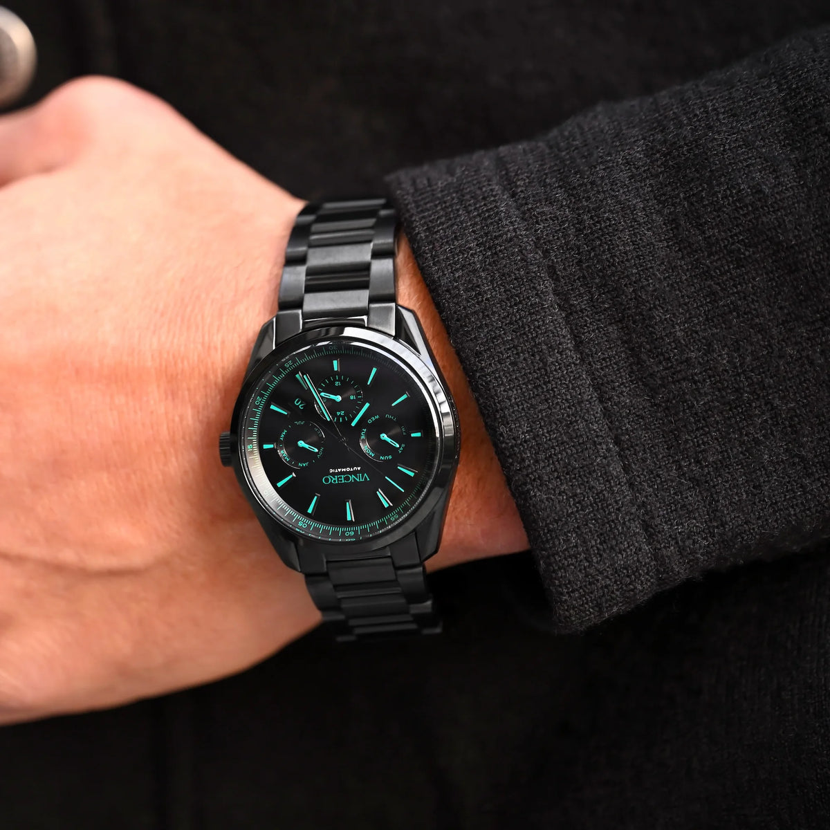 Black wristwatch with green accents on a person's wrist against a dark background