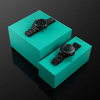 Two black watches on turquoise boxes against a dark background