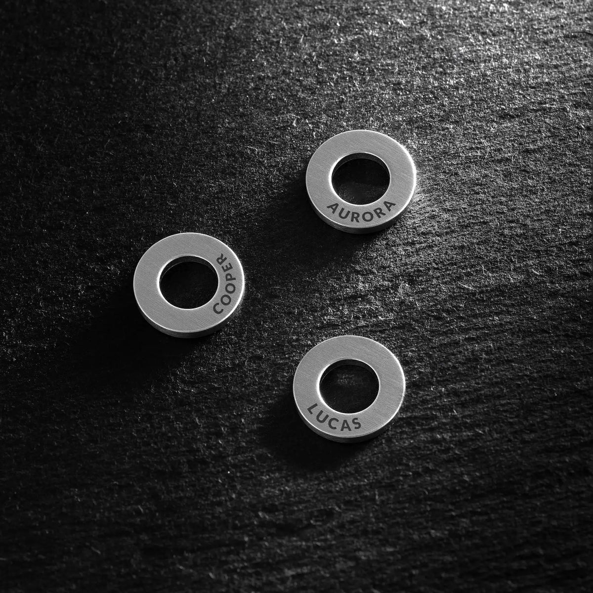 Three silver rings with engraved names on a dark textured surface