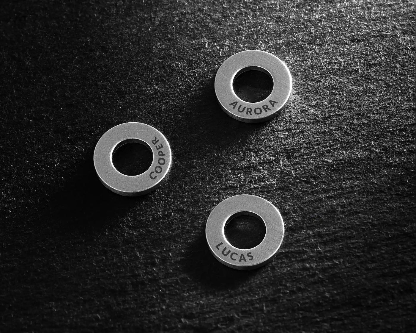 Three metallic rings with engraved names on a dark textured surface
