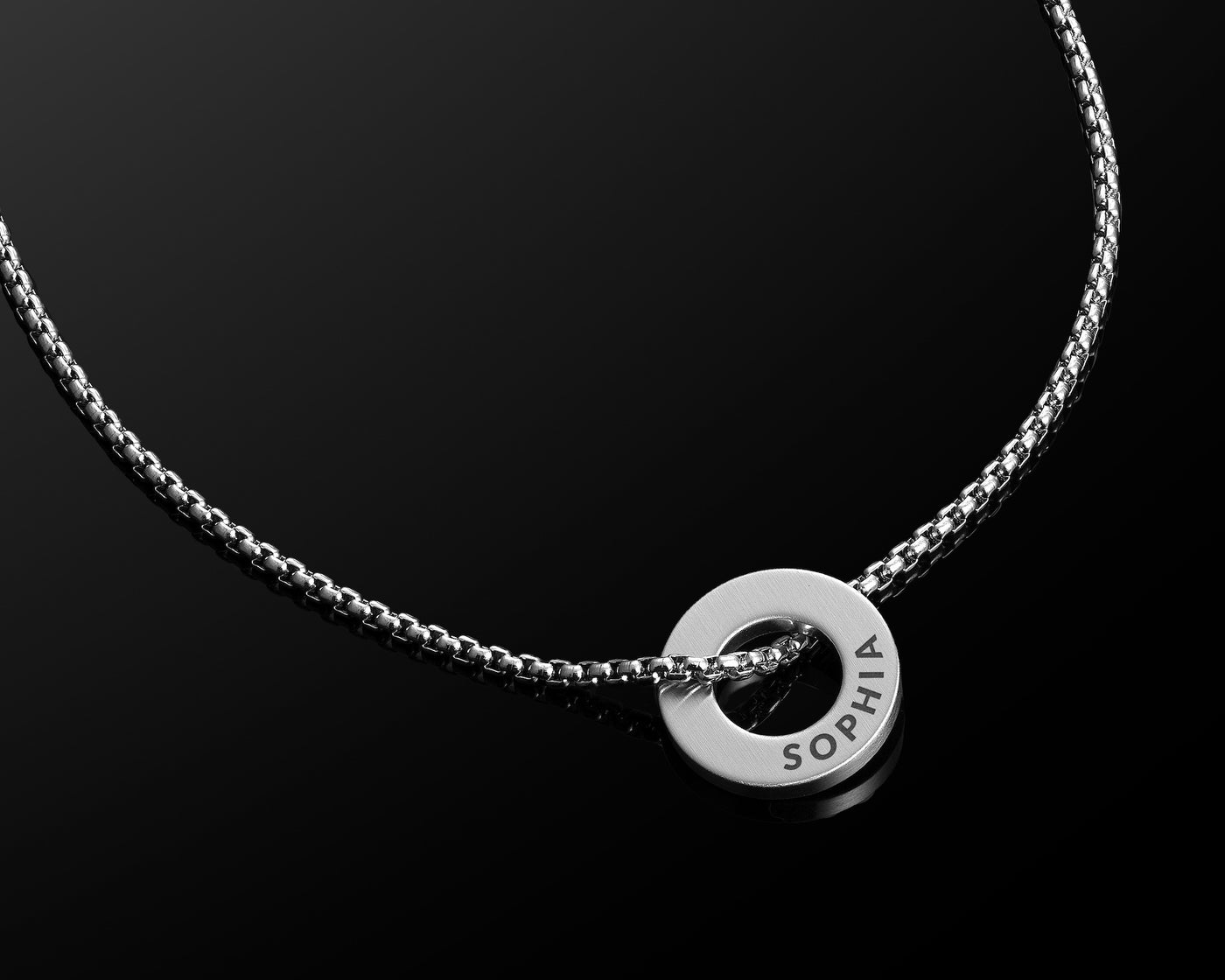 Silver necklace with a round pendant on a black background