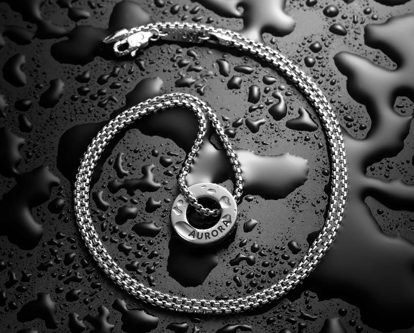 Silver chain necklace with a pendant on a wet surface