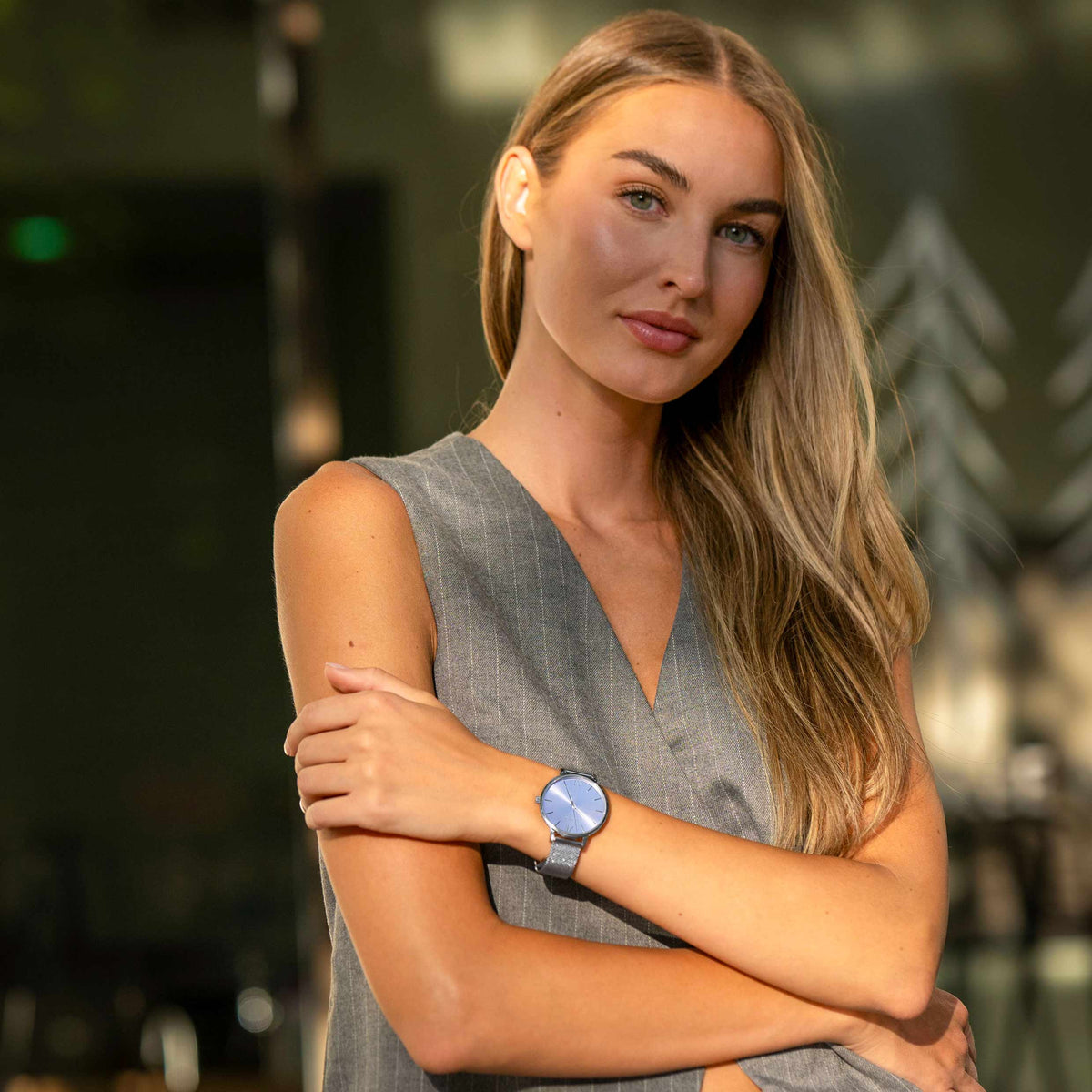 Woman wearing a gray sleeveless dress and a blue watch with a blurred background