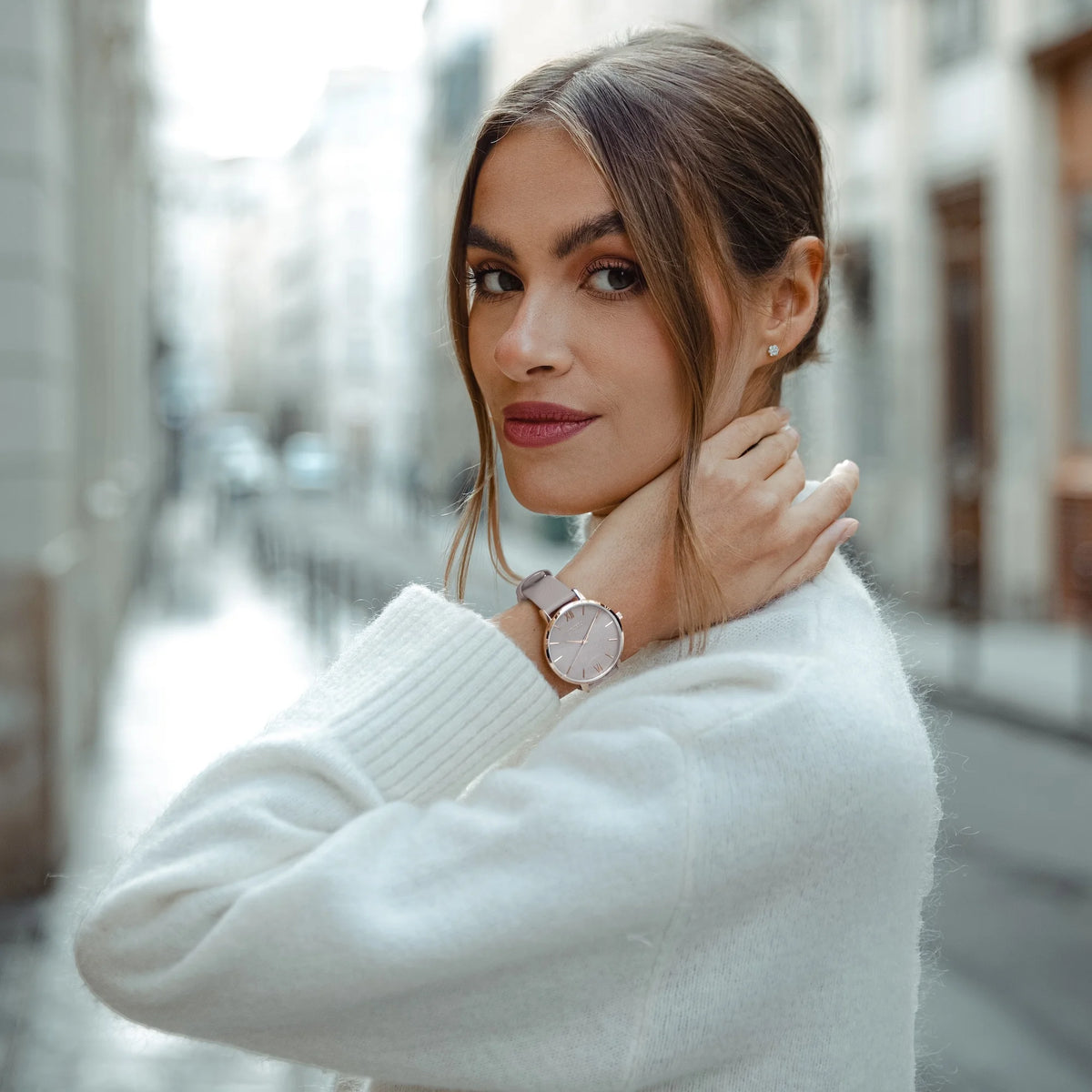Woman wearing a white sweater and a watch, standing in an outdoor setting.