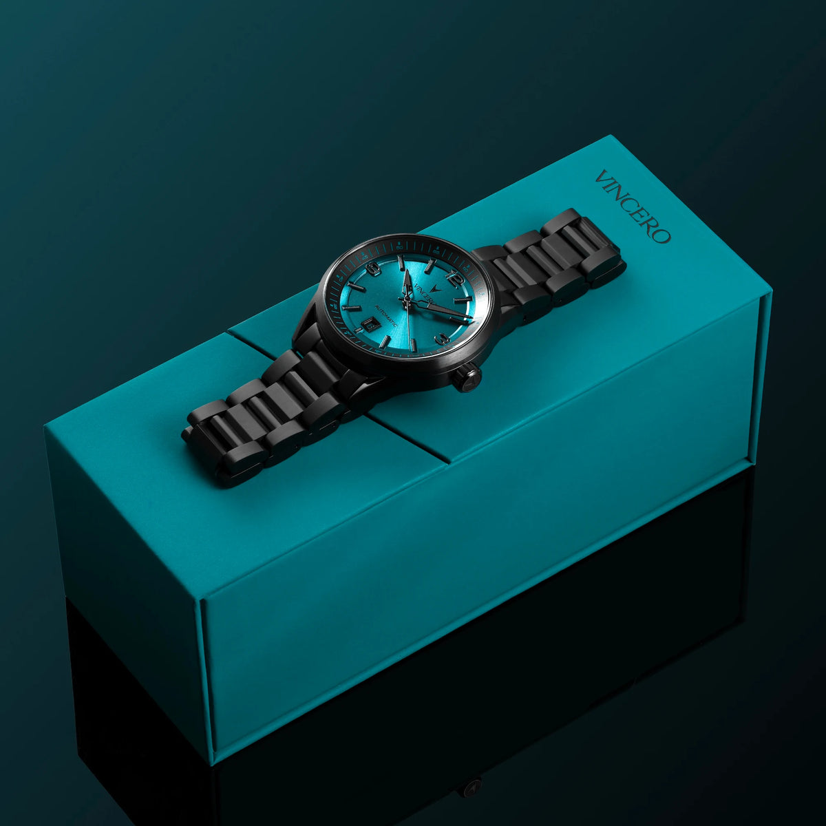 Black watch with blue glowing face on a teal box against a dark background