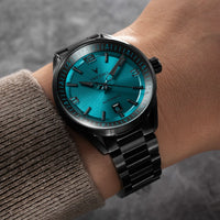 Wrist wearing a black watch with a blue face on a blurred background